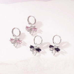 Detailed macro view showing butterfly bow hoop earrings with pink and dark purple zircons