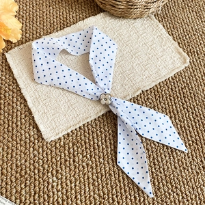 Close-up of white silk scarf necklace with blue polka dots and floral buckle.