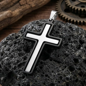 Gros plan d'un pendentif croix bicolore en acier inoxydable sur une pierre volcanique