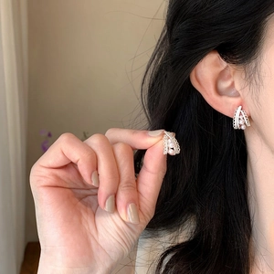 Close-up of elegant French pearl earrings shown worn on the ear and held by hand.
