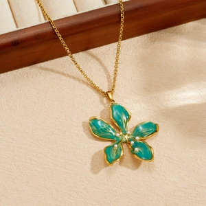 Dettaglio di una collana in acciaio dorato con pendente a fiore verde su espositore