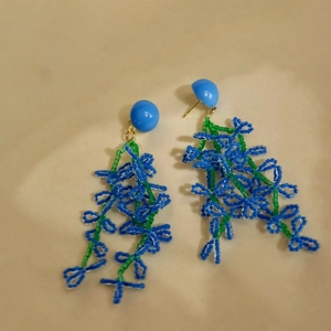 Dettaglio di orecchini pendenti con perline blu-verdi dal design floreale francese.