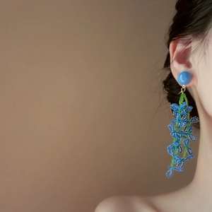Dettaglio ravvicinato di orecchini a nappa con fiori in perline blu e verdi su una modella