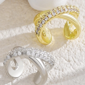Macro detail of gold and silver X-shaped crossover ear cuffs with pavé cubic zirconia