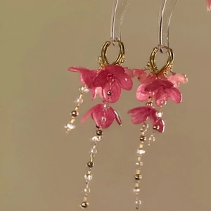 Detaillierte Nahaufnahme von rosa Blumen-Quastenohrringen mit Goldreifen und Perlenanhängern