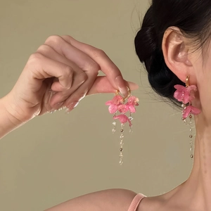 Nahaufnahme von rosa Blumen-Quastenohrringen mit goldener Schließe am Modell.