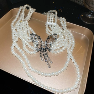 Détail d'un collier de perles à plusieurs rangs avec un pendentif papillon en strass sur plateau.