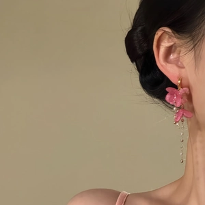Nahaufnahme der eleganten rosa Blumen-Quastenohrringe am Ohr mit zarten Blütenblättern.