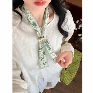 Elegant floral silk scarf necklace paired with a white linen shirt and green bag.