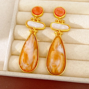Close-up of vintage resin drop earrings with marbled orange and amber textures in gold.