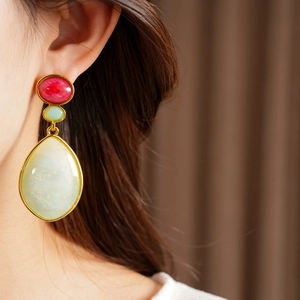 Detail view of vintage resin teardrop earrings with red and green stones on model.