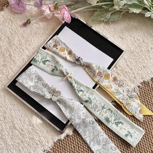 Close-up of three elegant floral silk scarf necklaces featuring decorative metal slides and charms