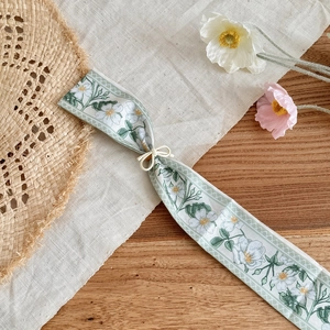 Detailed view of a slender silk scarf necklace featuring a delicate white floral pattern