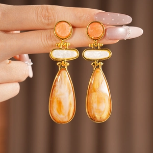 Close-up detail of elegant vintage teardrop earrings with marbled orange resin inlays