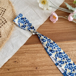 Close-up view of a blue floral silk scarf necklace with an adjustable pearl buckle