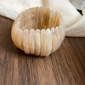 Close-up detail of beige marbled acrylic elastic bracelet on wooden surface