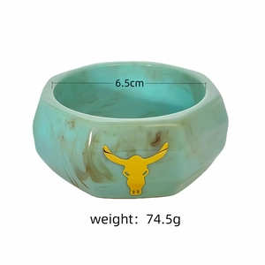 Gros plan sur un large bracelet y2k en résine marbrée sarcelle avec un charm tête de taureau jaune