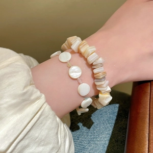 Primer plano de pulseras de cuentas de concha geométricas irregulares en la muñeca.