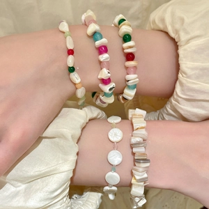 Vista detallada de varias pulseras de cuentas de concha de colores en la muñeca de una modelo