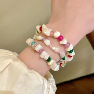 Detalle de tres pulseras de cuentas de concha irregulares y coloridas en una muñeca