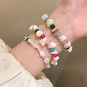 Vista detallada de tres pulseras de cuentas de concha irregulares de colores en una muñeca.