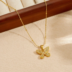 Dettaglio di una collana in acciaio inossidabile dorato con pendente a farfalla di cristallo.