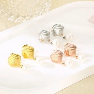Detailed view of three pairs of stainless steel shell and pearl earrings in gold, silver, and rose gold