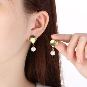 Close-up view of elegant gold shell stud earrings with white pearl drops on an Asian model.