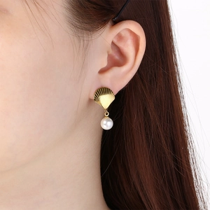 Detailed view of a golden stainless steel scallop shell earring with a white pearl