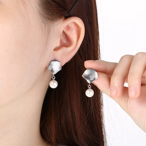 Close-up of silver shell earrings with pearls shown on a model's ear and in her hand
