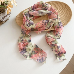 Close-up view of a vintage floral print mesh scarf draped on a textured decorative tray.