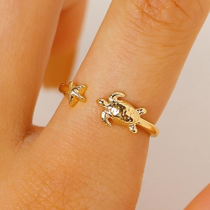 Primo piano di un anello dorato regolabile con motivi a tartaruga marina e stella marina.