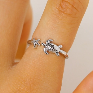 Dettaglio macro di un anello aperto in argento con tartaruga e stella marina al dito