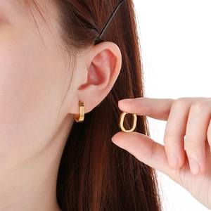 Close-up of gold U-shaped stainless steel hoop earrings worn on ear and held