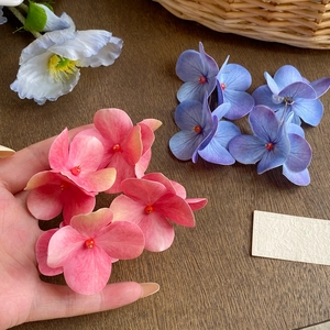 Hand holding large pink and blue hydrangea flower earrings on a rustic wood background