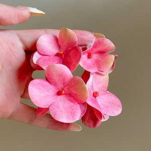 Close-up view of elegant pink hydrangea flower earrings held in hand showing fine petal texture