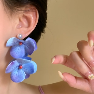Detail shot of elegant iris blue oversized floral drop earrings with white pearl studs