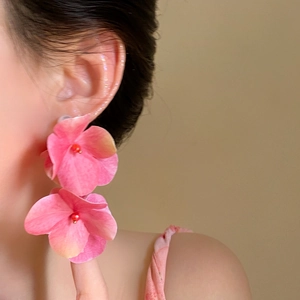 Macro view of oversized pink petal flower stud earrings worn by a model for summer