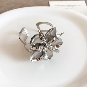 Dettaglio di un bracciale a polsino in metallo argentato con un fiore multistrato lucido
