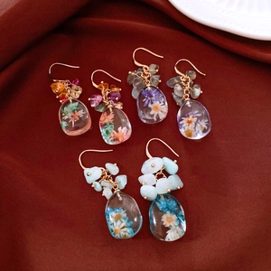 Close-up of handmade resin drop earrings featuring dried flowers and colorful gemstones.