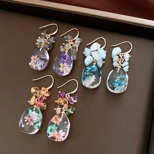 Close-up detail of handmade resin earrings featuring embedded dried flowers and natural stones.