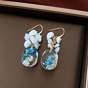 Close-up detail of resin teardrop earrings featuring preserved blue and white flowers inside.