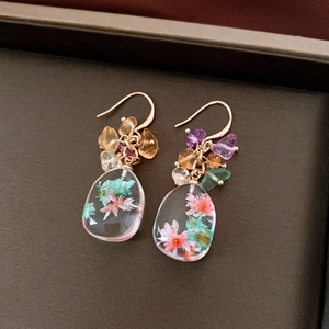 Detail of handmade resin drop earrings featuring real dried flowers and colorful gemstones