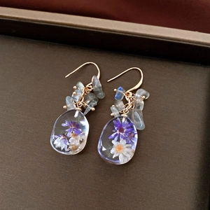 Macro detail of handmade resin earrings featuring real purple and white dried flowers and stones