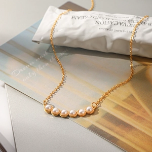 Primer plano de elegante collar de acero de titanio dorado con seis perlas blancas brillantes