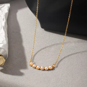 Detalle de un elegante collar de acero de titanio dorado con seis perlas blancas