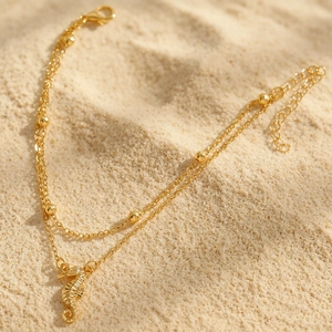 Detailansicht einer böhmischen goldenen doppelten Fußkette mit Seepferdchen auf Sand