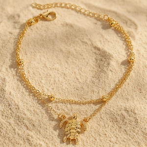 Detailansicht eines böhmischen goldenen Doppelfußkettchens mit Schildkrötenanhänger im Sand