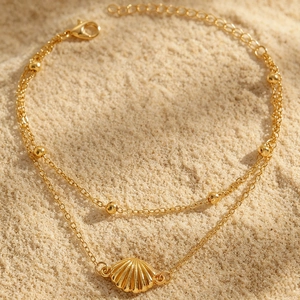 Detailansicht einer goldenen zweilagigen Muschel-Fußkette auf dem Sand.