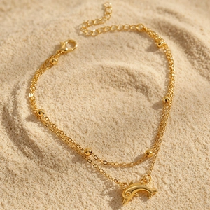 Detailansicht eines böhmischen doppellagigen Gold-Fußkettchens mit Delfin-Anhänger am Sand